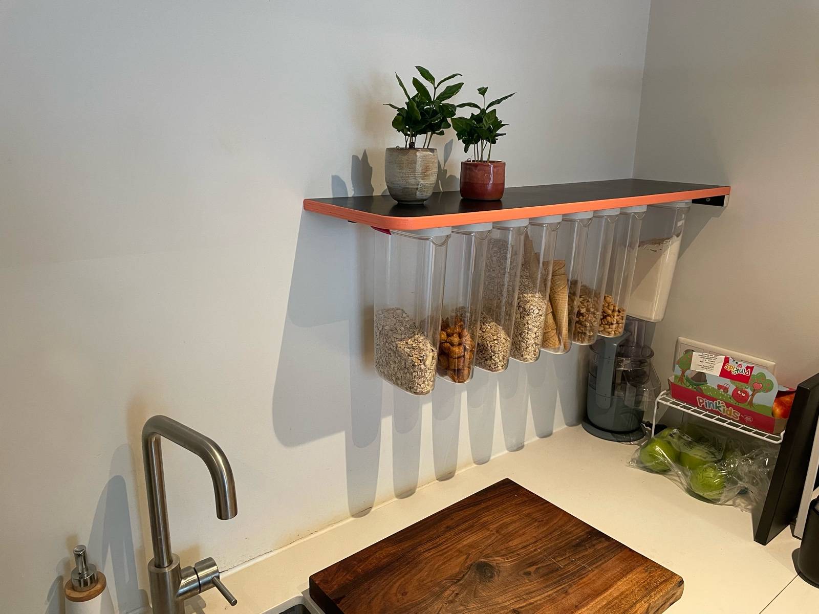 a black shelf with a painted orange/pink edge and Ikea food bins hanging off the bottom