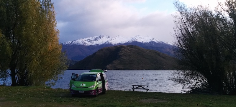 Camper van in front of lake, with snow-covered mountains in the background